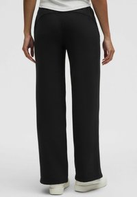 Pantaloni da tuta neri e a gamba larga, realizzati in tessuto morbido, con una vita liscia e una silhouette dritta, rifiniti con orli semplici.