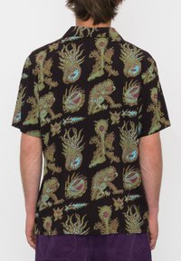 Chemise à manches courtes en tissu noir ornée de motifs colorés de dragons et de fleurs, avec une coupe décontractée et un col campagnard.