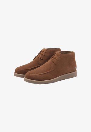 Stivali chukka in suede marrone con una texture morbida, dotati di chiusura con lacci, cuciture rinforzate e suola in gomma color beige.