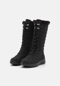 Botas negras de media caña hechas de un tejido suave con un diseño acolchado, que cuentan con cordones y acentos metálicos. Forro de felpa en la parte superior.