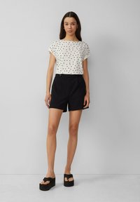 Top blanco de manga corta con lunares negros, combinado con pantalones cortos negros de cintura alta y sandalias de plataforma negras y voluminosas.