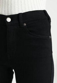 Svarta denimjeans med en åtsittande design, med silverfärgad knappstängning, sidofickor och en slät yta.