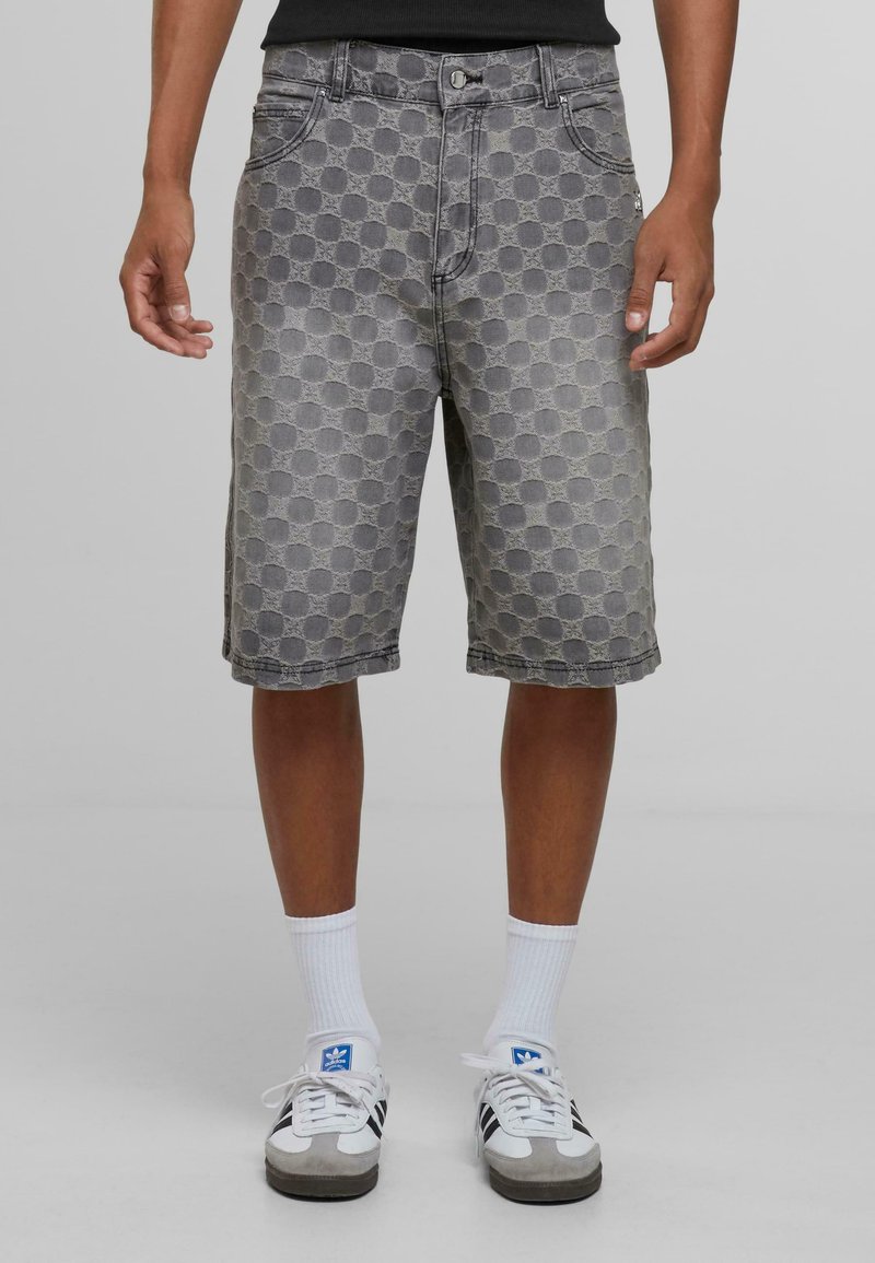Graue Jeans-Shorts mit einem strukturierten kreisförmigen Muster. Mittellange bis zur Mitte des Oberschenkels mit fünf Taschen und einem Gürtelschlaufen. Getragen mit weißen Socken und Turnschuhen.