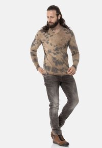 Beige Langarmshirt mit schwarzen Spritzmustern, kombiniert mit grauen engen Jeans und braunen Wanderschuhen.