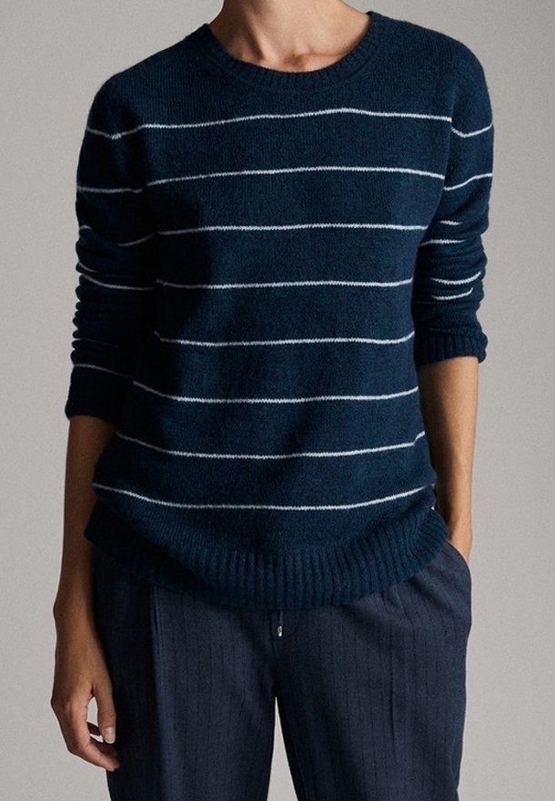 Personne portant un pull bleu marine avec des rayures horizontales blanches et un pantalon bleu marine à rayures, les mains détendues sur les côtés.