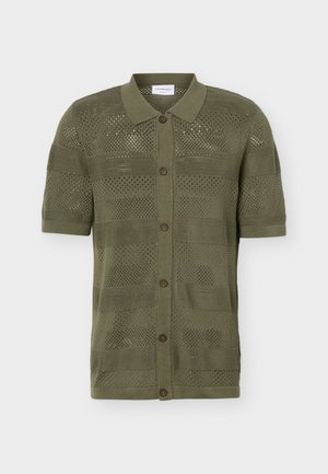 Krótki rękaw, oliwkowozielona dzianinowa koszulka polo z guzikami z przodu i ażurowym wzorem, wyłożona na płasko na białym tle.