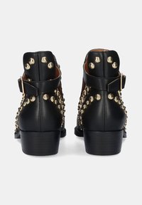 Botas de tobillo de cuero negro con tachuelas de metal dorado a lo largo de los lados, parte posterior cerrada y un tacón bajo apilado. Acento de hebilla en la correa del tobillo.