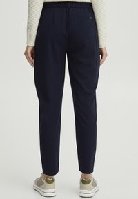 Navy tapered trousers with an elastic waistband and back pocket, made from smooth fabric. Worn with light-colored athletic shoes.