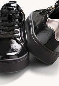 Fekete lakkbőr sportcipők textúrált fekete gumitalppal, fűzős kivitelben és fémes részlettel az oldalon.
