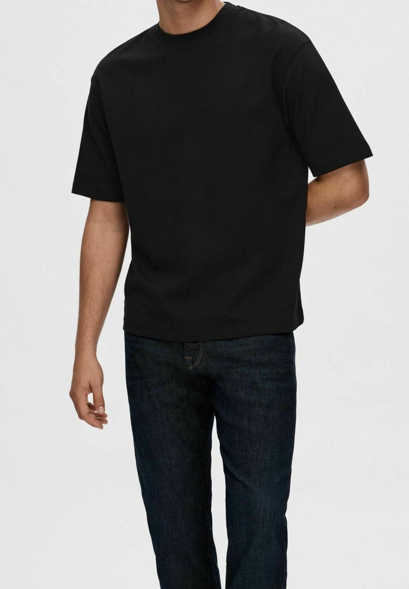 Black short-sleeve T-shirt made of cotton; round neck; paired with dark denim jeans with subtle texture and a standard fit.
