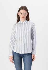 Pruhovaná košile na knoflíky v bílé a světle modré barvě, s límcem, dlouhými rukávy a vyšívaným logem na hrudi.