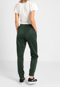 Gröna sportiga joggers med en avsmalnande passform, elastisk midja och manschetterade anklar, kombinerat med svarta sneakers mot en neutral bakgrund.