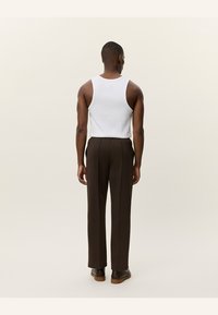 Weißes Tanktop von hinten sichtbar, kombiniert mit braunen Hosen. Glatter Stoff, lockere Passform und gerades Bein-Design, getragen mit dunklen Schuhen.