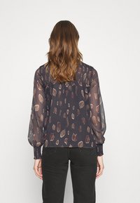 Blusa nera trasparente con un motivo leopardato in diverse tonalità di marrone, caratterizzata da maniche lunghe e dettagli arricciati ai polsini e nella parte posteriore.