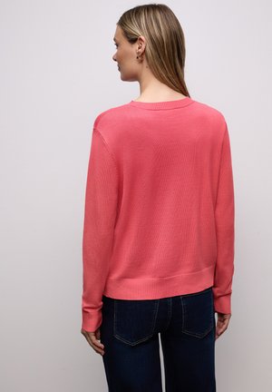 Pull corail à coupe décontractée, col et poignets côtelés. Design style sweat-shirt, associé à un jean bleu foncé. Tissu doux et texturé.
