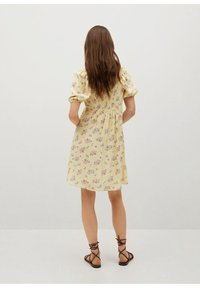 Vestido floral amarillo con mangas cortas abullonadas, corsé ajustado y falda fluida. Tela ligera con pequeños patrones florales y detalles elásticos.