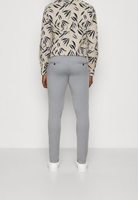 Light gray pants with a slim fit, featuring a smooth texture and back pockets. Worn with a patterned long-sleeve shirt.