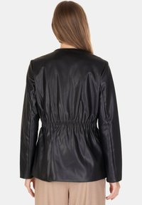 Giacca in finta pelle nera con vita aderente, maniche lunghe e texture liscia, vista da dietro.