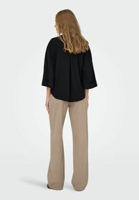 Sort oversized skjorte med trekvart ærmer, parret med løse beige bukser med hvide prikker, set fra ryggen.