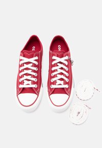 Κόκκινα πάνινα αθλητικά παπούτσια με λευκές λαστιχένιες σόλες και προφυλακτήρες στα δάχτυλα. Διαθέτουν λευκά κορδόνια, ασημί μεταλλικά στοιχεία και περιλαμβάνουν επιπλέον λευκά και κόκκινα κορδόνια.