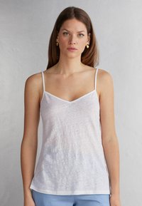 Witte, lichte cami met dunne bandjes en een V-hals ontwerp. Heeft een licht doorzichtig textuur en een relaxte pasvorm.