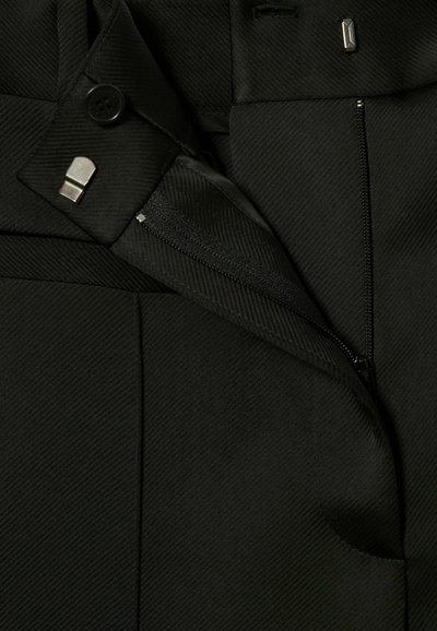 Pantaloni neri su misura realizzati in tessuto texturizzato, con coste diagonali, una tasca con zip e dettaglio di chiusura con bottone.