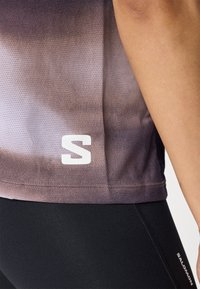 Lilla gradient treningsskjorte med mesh-struktur, med en hvit "S" logo på nedre venstre side, parret med svarte leggings.