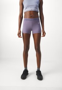 Nike Pro shorts lilac dengan pinggang elastis yang menampilkan "NIKE PRO" dalam warna yang lebih gelap; dipadukan dengan atasan crop abu-abu dan sepatu olahraga hitam.