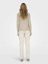 Hellbeige Langarmshirt mit lockerem Schnitt, kombiniert mit cremefarbenen Hosen. Das Shirt hat eine weiche Textur und einen abgerundeten Saum.