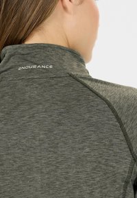 Nærbillede af en persons ryg iført en grå atletisk top med "ENDURANCE" trykt på den høje krave, som viser syningsdetaljer.