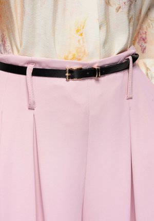 Ceinture noire mince avec boucle dorée sur une jupe taille haute rose clair, associée à un chemisier crème arborant un motif floral délicat.