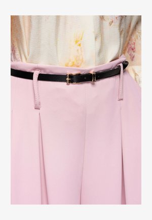 Cinturón negro delgado con hebilla dorada sobre falda de talle alto en rosa claro, combinado con blusa crema con suave estampado floral.