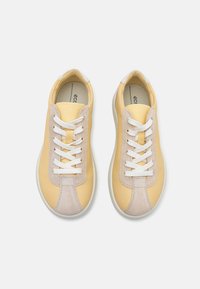 Sneakers in pelle con una tomaia gialla pallido, rifinita con accenti in suede beige e lacci bianchi. Punta arrotondata e suola in gomma con texture.
