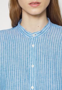 Modrá a bílá pruhovaná košile s mandarínským límcem, vyrobená z lehké, texturované látky a s několika knoflíkovými zapínáními vpředu.