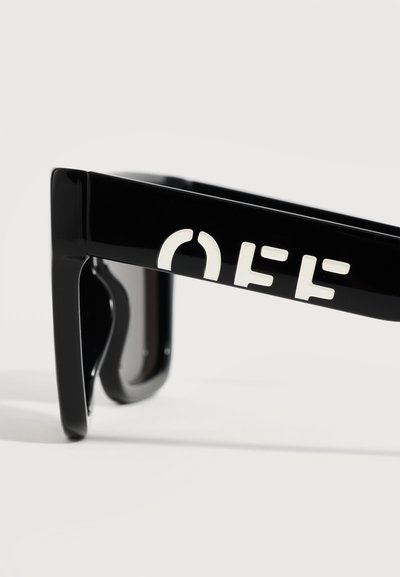 Branché de lunettes de soleil noir avec des lettres blanches stylisées en gras formant le mot « OFF » sur un fond clair uni.