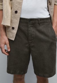 Dark green shorts made of textured fabric, featuring a button closure, side pockets, and a relaxed fit. Worn with a light shirt and sweater.
