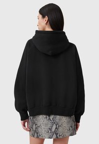 Sudadera negra con capucha, de corte relajado y puños acanalados. Combinada con una falda de estampado de serpiente, que muestra texturas contrastantes.