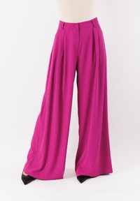 Pantaloni larghi fucsia realizzati in tessuto morbido, con vita alta, pinces e chiusura a un bottone. Accentuati da scarpe nere.