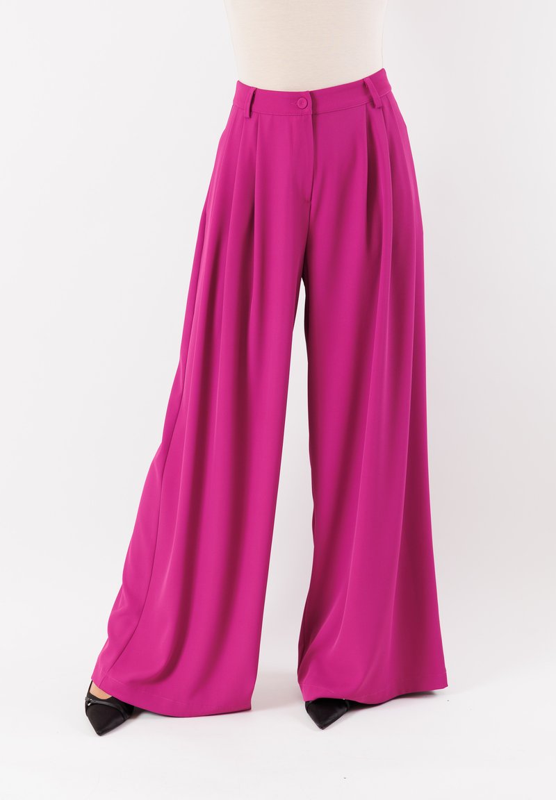 Pantaloni larghi fucsia realizzati in tessuto morbido, con vita alta, pinces e chiusura a un bottone. Accentuati da scarpe nere.