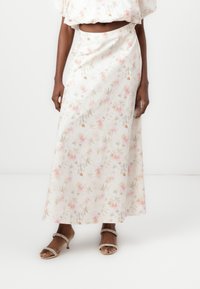 Gonna maxi in tessuto leggero con motivo floreale. I colori includono bianco, rosa e verde chiaro. Presenta una vita alta e un design fluido.
