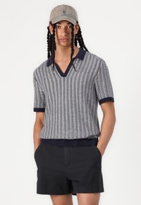 Polo shirt tricot à manches courtes en bleu marine et blanc, doté d'un col en V et d'arêtes côtelées. Associé à un short noir, à la fois décontracté et ajusté.