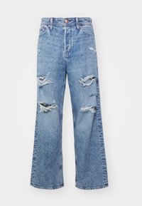 Jeans en denim bleu clair avec une coupe décontractée, présentant des patches distendus et des déchirures à l'avant. Ourlet cousu et design classique à cinq poches.