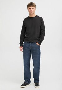 Črn bombažni pulover z dolgimi rokavi, okroglim izrezom, v kombinaciji z modrimi jeans hlačami in črnimi športnimi copati. Preprost dizajn, brez vzorcev ali logotipov.