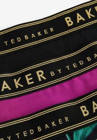 Crne i magenta elastične trake s zlatnim natpisom. Gornja traka prikazuje "TED BAKER", dok srednja traka ističe "BAKER."