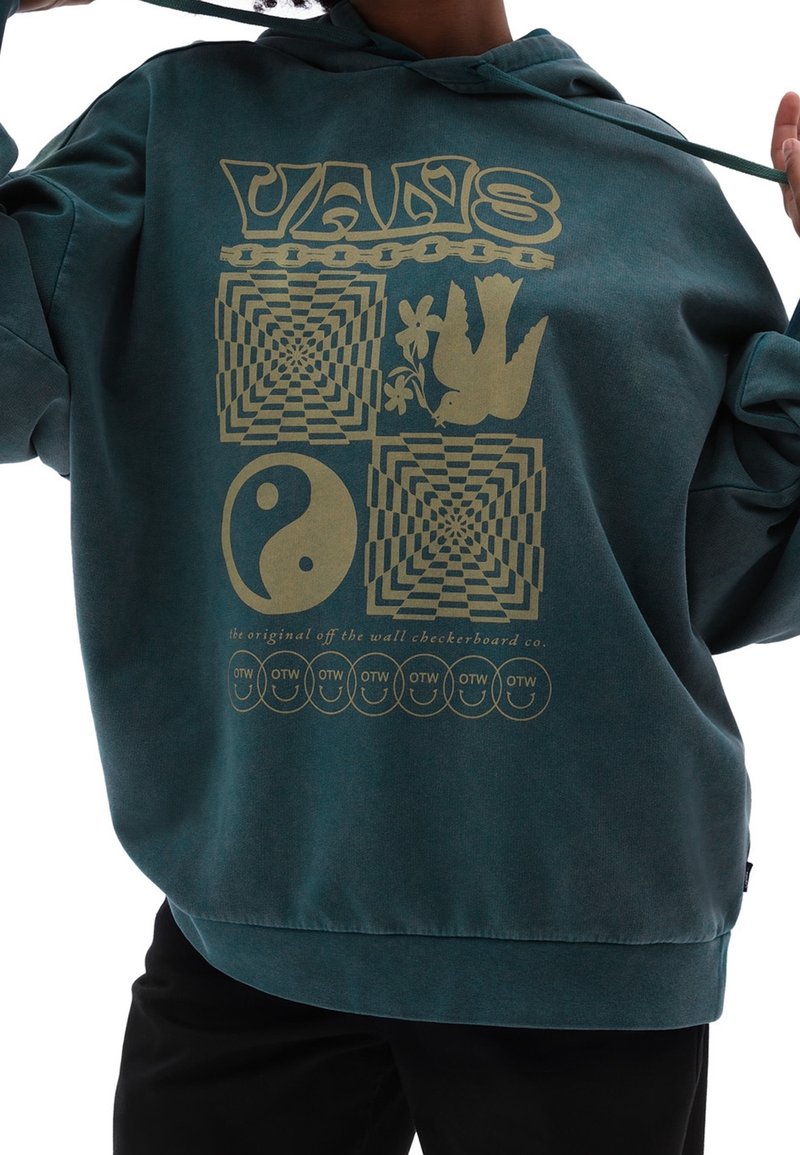 Personne portant un sweat à capuche bleu sarcelle avec un motif jaune du logo Vans, des motifs damier, une colombe tenant des fleurs, un symbole yin-yang, et des visages souriants OTW.