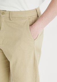 Beige katoenen broeken met een ontspannen pasvorm, voorzien van zijzakken, subtiele stiksels en een vlakke voorkant.