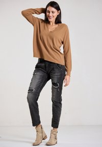 Brown V-neck sweater, knitted, paired with black distressed jeans. Worn with beige ankle boots featuring a side buckle detail.