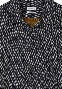 Camicia a maniche corte con colletto di colore blu navy, decorata con un motivo geometrico bianco e arancione. Presenta bottoni scuri e un tessuto morbido e strutturato.