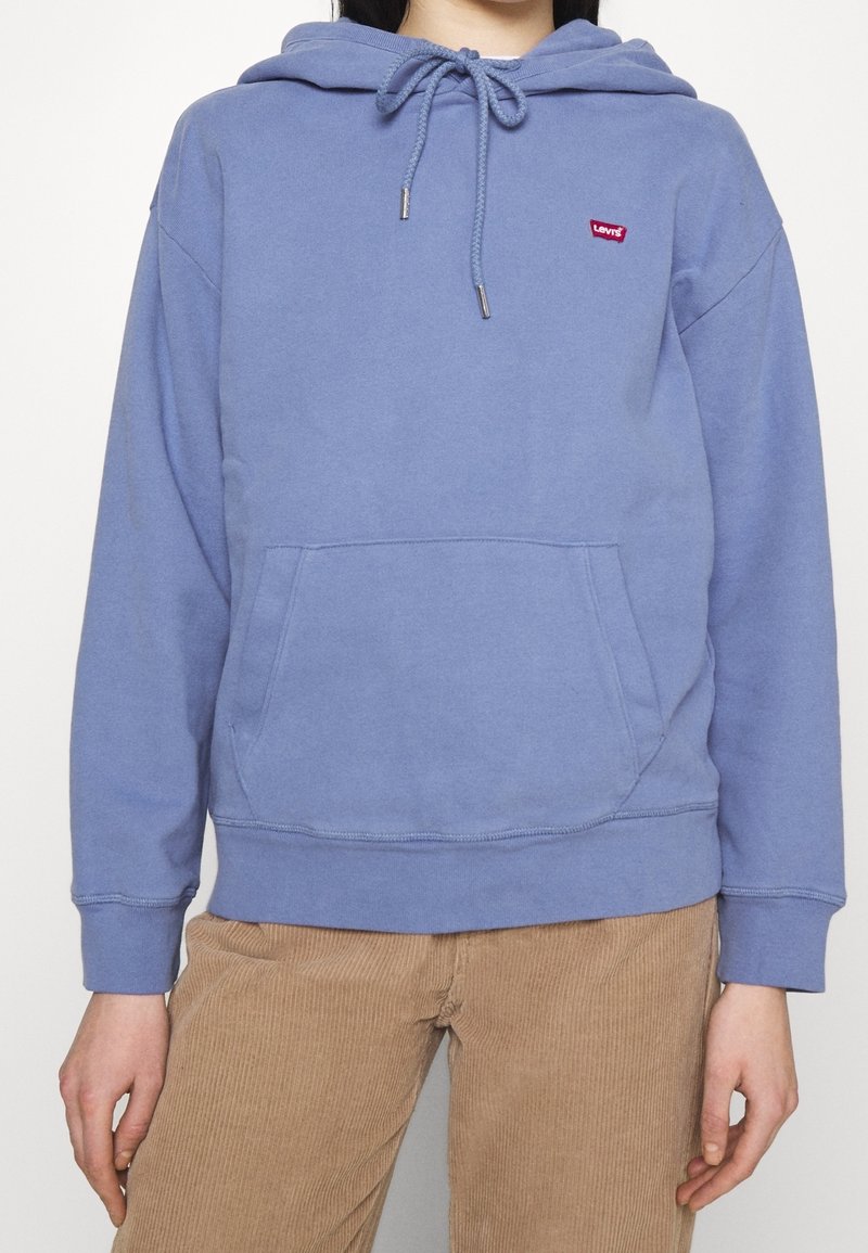 Sudadera con capucha azul claro con bolsillo canguro frontal, cordón ajustable y parche de logo rojo. Material suave con puños y dobladillo acanalados.