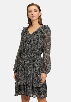 Zwart-wit polkadotjurk met ruches bij de halslijn, lange doorschijnende mouwen en een gelaagde rok. Gemaakt van lichtgewicht, vloeiend materiaal.